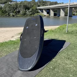 Front view of a pre-owned carbon eFoil board standing upright near the water.